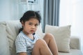 Asian kid girl upset lonely bullied little looking at camera feels abandoned abused, sad alone sitting on the sofa couch in living Royalty Free Stock Photo