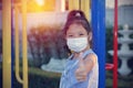 Asian kid girl wearing a medical mask protect coronavirus, sitting alone, looking at the camera in the garden show thumbs up for