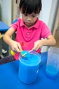 Asian kid holding spoon of blue chemical, Copper Sulphate Pentahydrate, against blue table