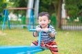 Asian kid riding seesaw board at the playground under sunlight,