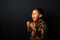 An Asian kid wearing Batik is screaming isolated on black background Royalty Free Stock Photo