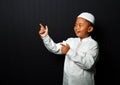 An Asian kid wearing a cap points his hand to the empty space isolated on black background Royalty Free Stock Photo