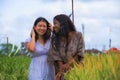 Asian Korean girl and black African American woman exploring together exotic tropical village on fresh rice field enjoying