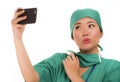 Asian Korean woman as successful taking selfie on hand phone - young beautiful and happy medicine doctor or hospital nurse taking Royalty Free Stock Photo