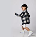 Asian kid boy in sunglasses, plaid cardigan and white shorts walks run out of camera over background with copy space