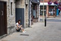 An Asian lady in her twenties looking at her mobile phone whilst sat on a step outside a shop