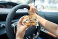 Asian lady holding hamburger to eat in car, dangerous and risk an accident