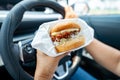 Asian lady holding hamburger to eat in car, dangerous and risk an accident