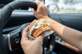 Asian lady holding hamburger to eat in car, dangerous and risk an accident