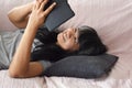 Asian lady with natural black and gray hair colours lying on a sofa using a smartphone at home.