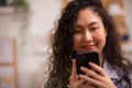 Asian lady sits on sofa at home, texting and talking with buddy, holding smartphone, shopping online, or checking mobile app or Royalty Free Stock Photo