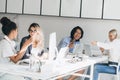 Asian laughing man making selfie with blonde girl in office while charming ladies beside talking with each other. Indoor