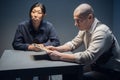 Asian lawyer and a bald investigator prepare to interrogate a suspect while sitting at a table