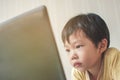 Asian little boy be stern looking into a laptop screen.
