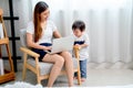 Asian little boy play near his mother use laptop to work in room of their house with white curtain and day light Royalty Free Stock Photo