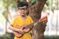 An Asian little boy wearing glasses is happily playing the ukulele. Asian little child is trying to play the ukulele with a fully Royalty Free Stock Photo