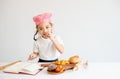Asian little chef girl test the taste of bread on the table by pick some piece and eat with white background