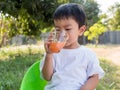 Asian little child boy drinking orange juice from glass outdoor nature background Royalty Free Stock Photo