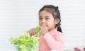 Asian little child girl eating green vegetable salad using hands with happy face at home. Healthy food in children. White Royalty Free Stock Photo