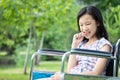 Asian little child girl feeling stressed,worried female bites finger nails in wheelchair outdoor park,girl patient with nervous