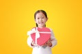 Asian little child girl holding red heart gift box isolated on yellow background. Kid giving red heart gift box for you. Concept Royalty Free Stock Photo