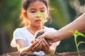 Asian little child girl and parent planting young seedlings in the black soil together in the garden