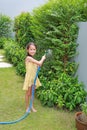 Asian little child girl pouring water spray on trees. Kid watering plants in the garden near his house Royalty Free Stock Photo