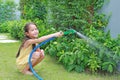 Asian little child girl pouring water spray on trees. Kid watering plants in the garden near his house Royalty Free Stock Photo