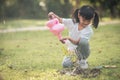Asian little child girl pouring water on the trees. kid helps to care for the plants with a watering can in the garden Royalty Free Stock Photo