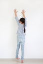 Asian little child girl raise hand up and climbing posture at white wall of room. Back view