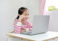 Asian little child girl sitting at desk enjoy watching cartoon on laptop computer stay at home Royalty Free Stock Photo