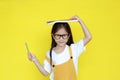 Asian little child girl wearing glasses with book on head and holding pencil with smiling isolated on yellow background. Portrait Royalty Free Stock Photo