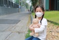 Asian little child girl wearing mask to protect corona virus and air pollution dust with hugging teddy bear doll sitting outdoor. Royalty Free Stock Photo