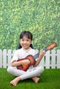 Asian Little Chinese girl sitting on grass and playing with guitar Royalty Free Stock Photo