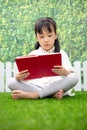 Asian Little Chinese girl sitting on the grass and reading book Royalty Free Stock Photo