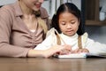 Asian little cute girl learning and studying her lesson with mother at home, schoolgirl pupil doing homework with tutor teacher, Royalty Free Stock Photo