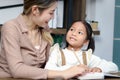 Asian little cute girl learning and studying her lesson with mother at home, schoolgirl pupil doing homework with tutor teacher, Royalty Free Stock Photo