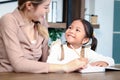 Asian little cute girl learning and studying her lesson with mother at home, schoolgirl pupil doing homework with tutor teacher, Royalty Free Stock Photo