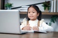 Asian little cute girl using laptop computer for online lesson, schoolgirl pupil distance learning online and doing homework at Royalty Free Stock Photo