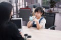 Asian little asian girl child is holding blue piggy bank and bring money deposit with woman Bank clerk in Thailand. Child is