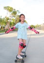 Asian little girl child skateboarder wearing safety and protective equipment playing on skateboard. Kid skateboarding on the road