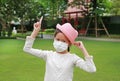 Asian little girl child wearing medical mask and straw hat with pointing one forefinger up due covid-19 on the garden Royalty Free Stock Photo