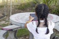 Asian little girl with dark braid is sitting and enjoying playing games on tablet in garden outdoors.