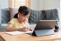 Asian little girl doing homework, learning, student using digital tablet. Homeschooling, Concept online learning at home