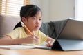 Asian little girl doing homework, learning, student using digital tablet. Homeschooling, Concept online learning at home