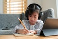 Asian little girl doing homework, using digital tablet with headphone. Homeschooling, Concept online learning at home Royalty Free Stock Photo