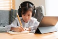 Asian little girl doing homework, using digital tablet with headphone. Homeschooling, Concept online learning at home Royalty Free Stock Photo