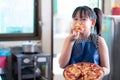 Asian little girl eating pizza with delicious and happiness after making homemade pizza in the home kitchen Royalty Free Stock Photo