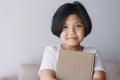 Asian  little girl is hold a brown book and smiling while standing in the living room at her home Royalty Free Stock Photo