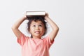 Asian little girl holding a book on head and eyes looking top on white background head. On face a cute girl so happy and smile